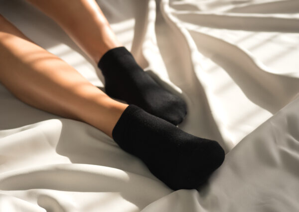 schwarze Sneakersocken Frauenfüße auf Bett